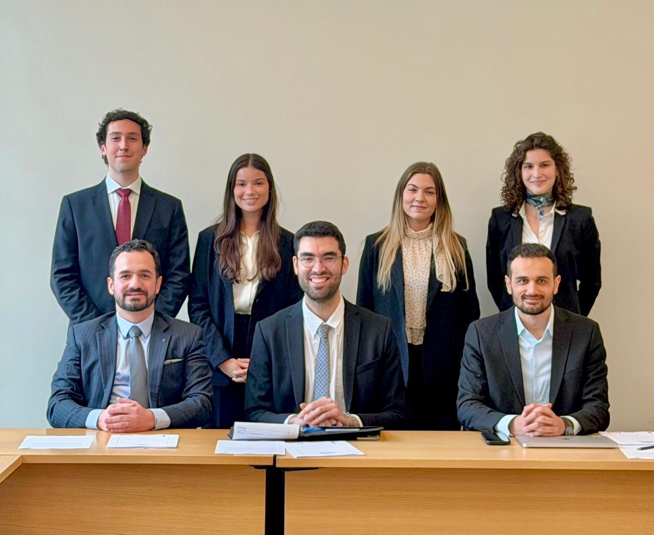 Retrato grupal de siete profesionales y estudiantes vestidos de traje en un entorno académico formal.