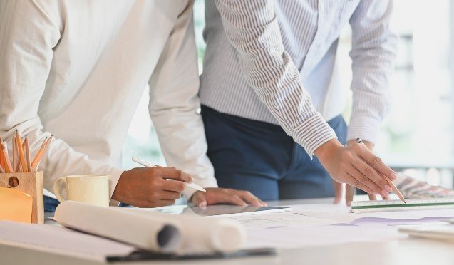 Dos personas escribiendo sobre planos ubicados en una mesa