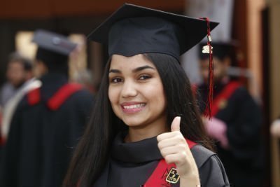 Estudiante con toga y birrete el día de su graduación levanta el dedo pulgar de la mano