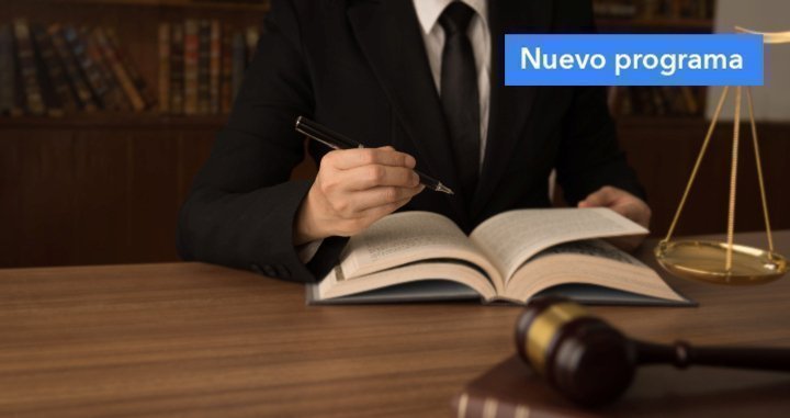 Plano medio de torso de persona con vestido de abogado escribiendo sobre cuaderno en un escritorio, al lado se ve un péndulo de la justicia