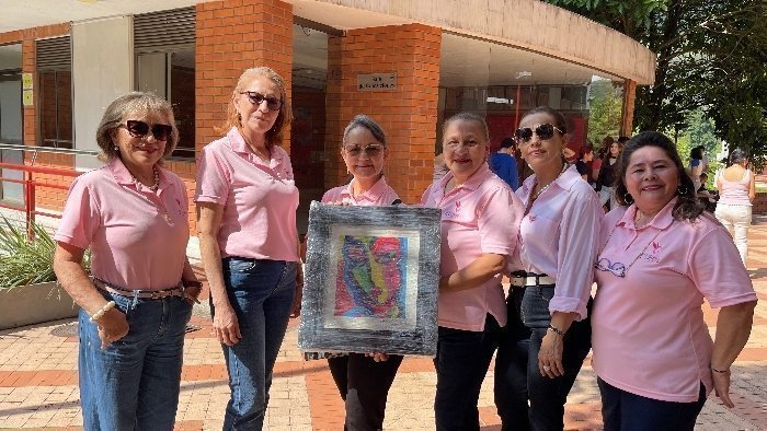 Mujeres con un cuadro y vestidas de rosado posan para una fotografía