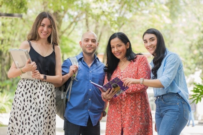 Grupo de cuatro jóvenes sonrientes caminando al aire libre con cuadernos.