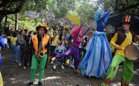 personaje de la comparsa tocando saxofón y otro tambor. Al fondo se ven los estudiantes