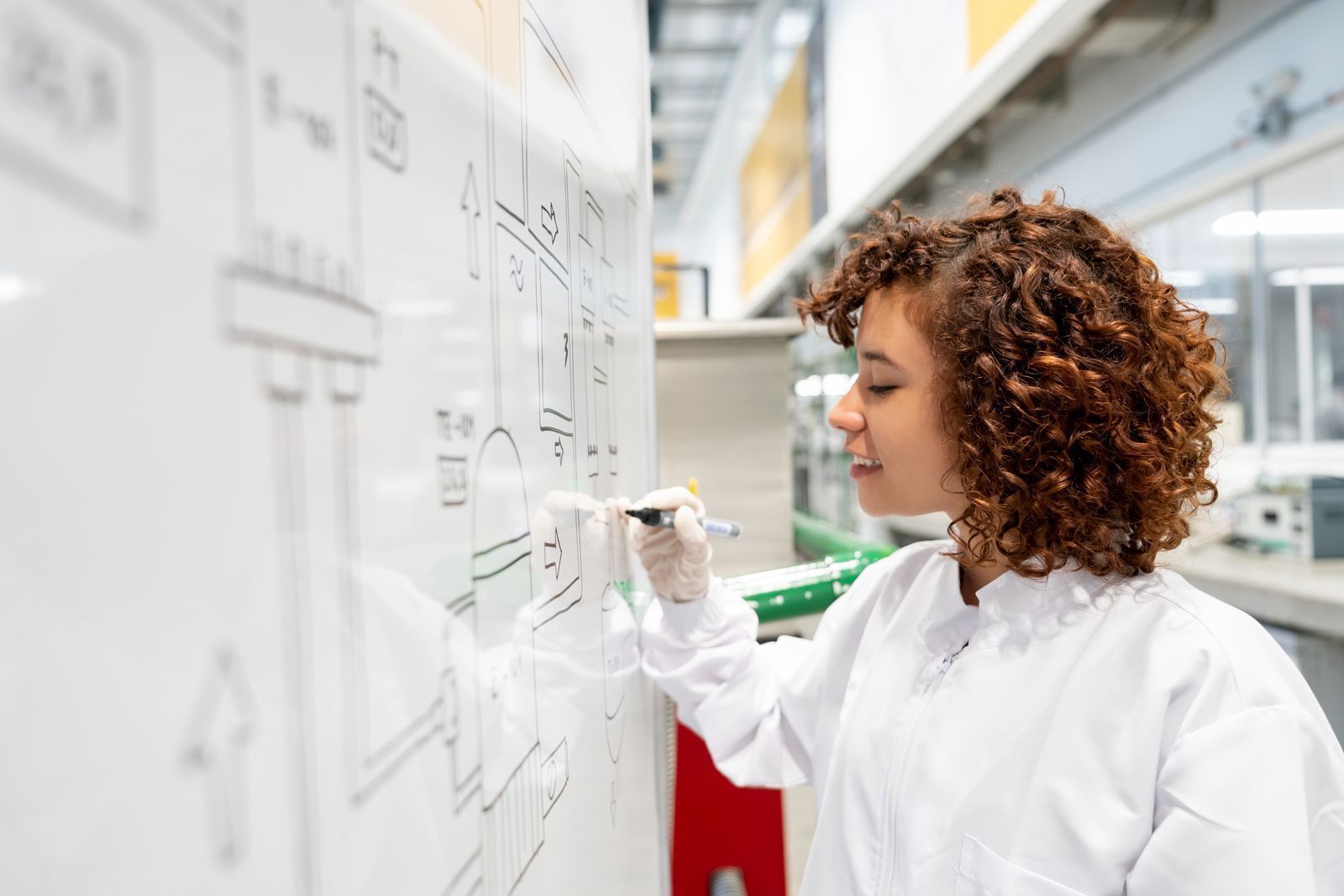 Mujer con vestuario de laboratorio escribiendo en tablero