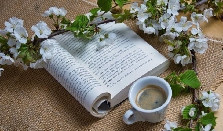 Libro abierto en mesa rodeado de flores y una tasa de te