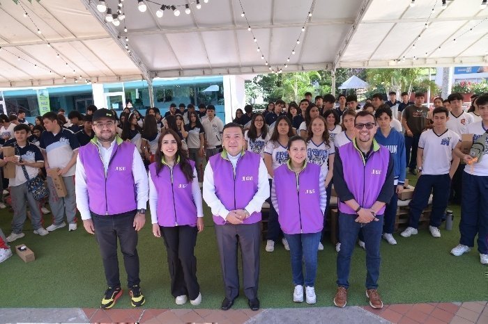 Directivos y docentes UPB posan para una fotografía. Hay estudiantes de colegios al fondo. 