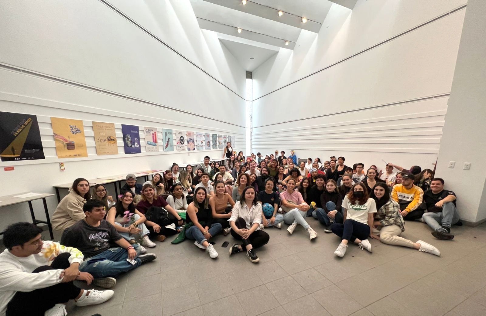 Grupo grande de estudiantes sentado y de pie en un vestíbulo moderno, sonriendo y mirando a la cámara.